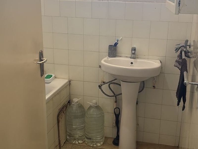A dated bathroom featuring a pedestal basin and bathtub with tiled finishes, requiring renovation to address worn surfaces and exposed plumbing.