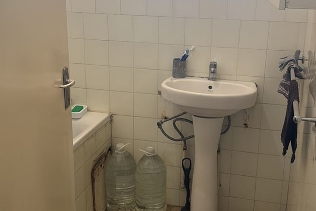 A dated bathroom featuring a pedestal basin and bathtub with tiled finishes, requiring renovation to address worn surfaces and exposed plumbing.