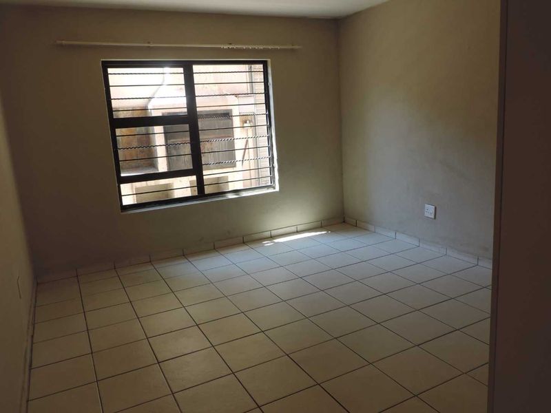 An empty bedroom featuring tiled flooring and a window fitted with security bars, offering a blank canvas for personalization.