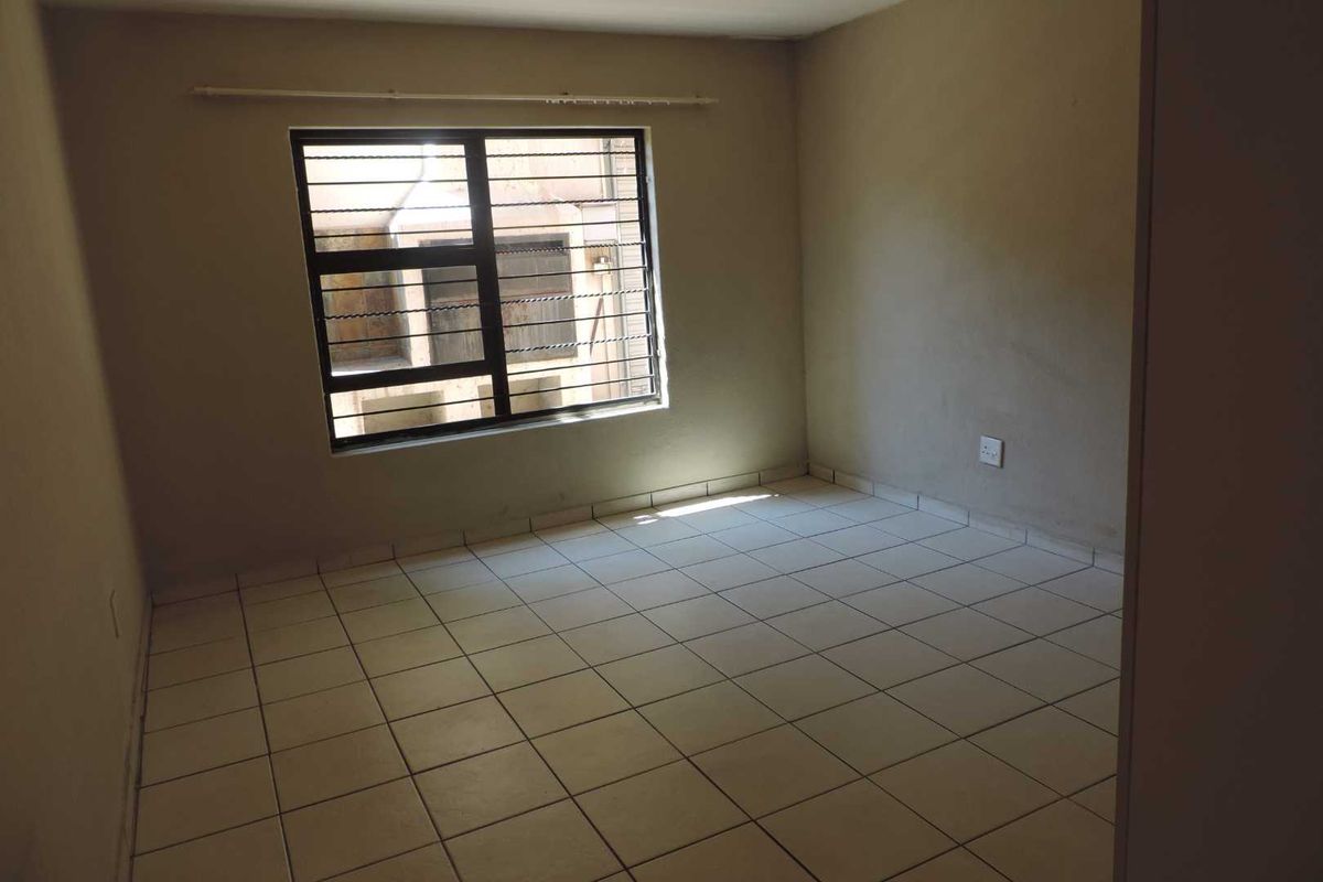 An empty bedroom featuring tiled flooring and a window fitted with security bars, offering a blank canvas for personalization.