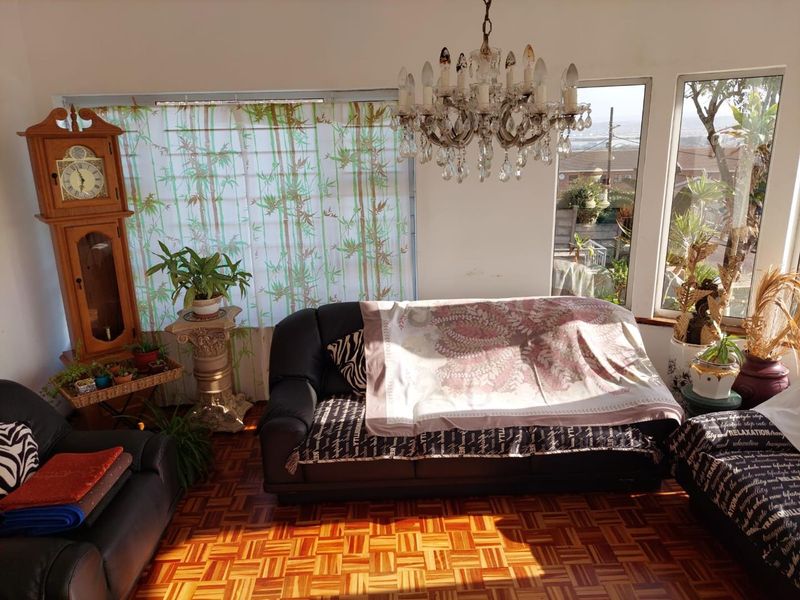 A living room featuring classic parquet flooring, a decorative crystal chandelier, and large windows providing natural light and exterior views.