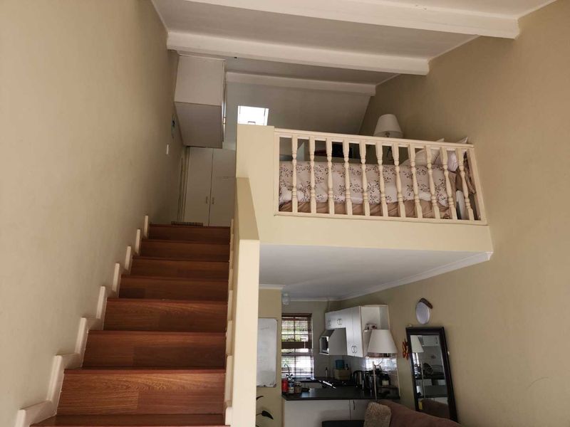 Open plan living area featuring a wooden staircase leading to a mezzanine bedroom level with a balustrade and integrated kitchen cabinetry below.