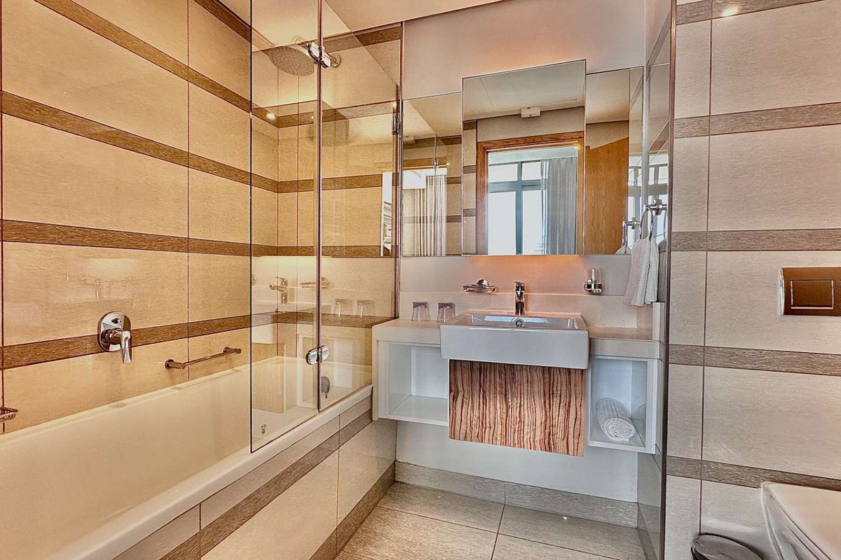 Modern bathroom featuring a wall-mounted basin, built-in bathtub with glass screen, and neutral tiled finishes throughout.