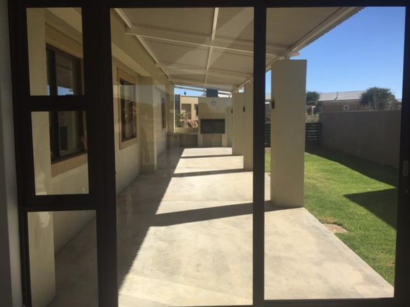 A spacious covered patio featuring a built-in braai, concrete flooring, and direct access to the garden through large sliding glass doors.