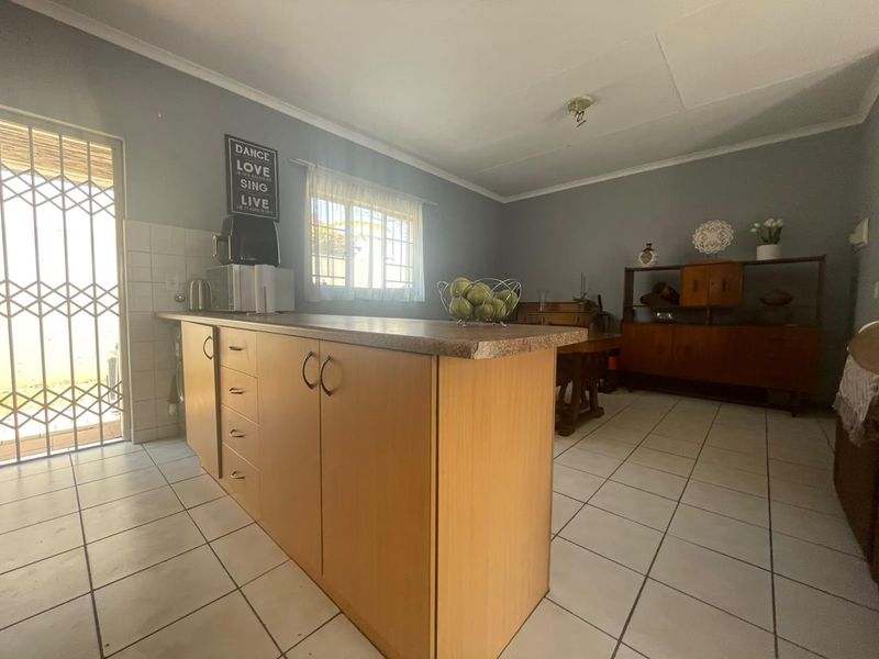 A functional kitchen area featuring a central island with laminate countertops, tiled flooring, and direct access to an exterior security gate.