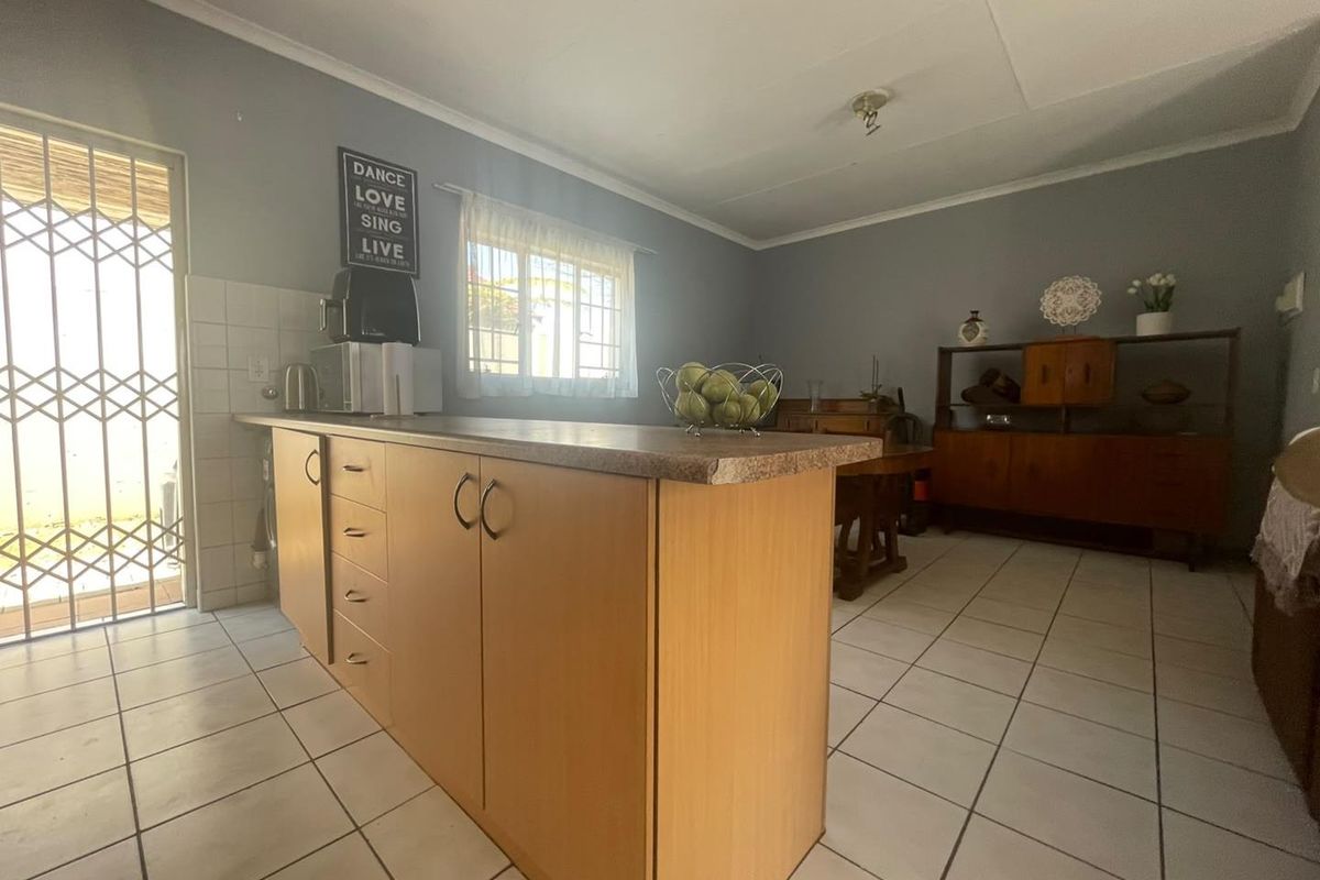 A functional kitchen area featuring a central island with laminate countertops, tiled flooring, and direct access to an exterior security gate.