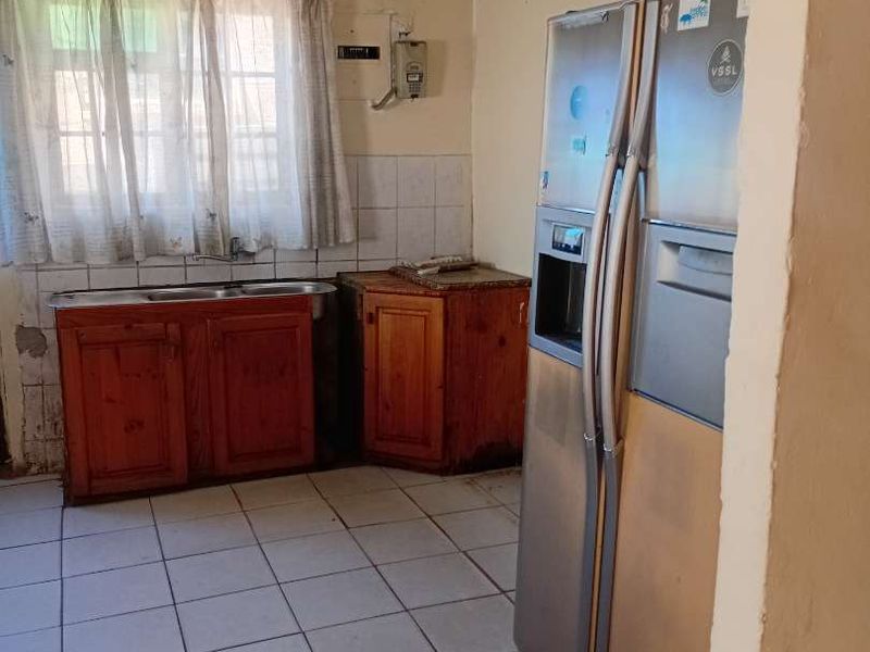 A dated kitchen featuring wooden cabinetry, a double sink, and tiled flooring, currently requiring significant cosmetic renovation and repairs to the ceiling and walls.