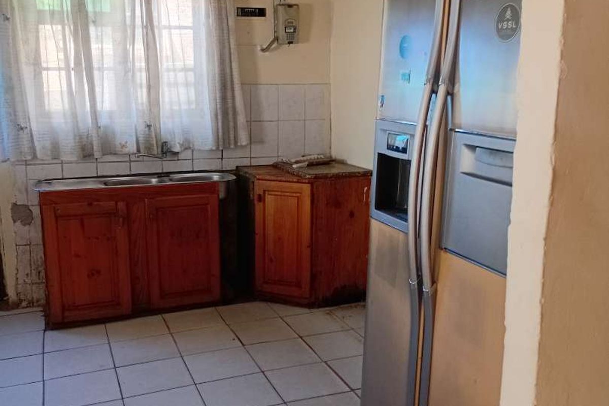 A dated kitchen featuring wooden cabinetry, a double sink, and tiled flooring, currently requiring significant cosmetic renovation and repairs to the ceiling and walls.