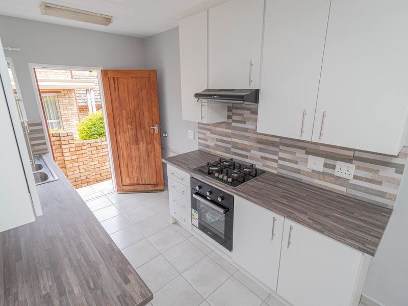 A clean, functional kitchen featuring white cabinetry, dark laminate countertops, a gas hob, built-in oven, and direct access to the exterior.