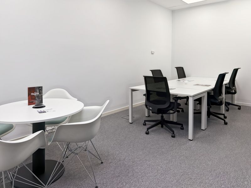 A clean, modern office space featuring neutral walls, carpeted flooring, and recessed ceiling lighting, suitable for professional meetings or collaborative work.