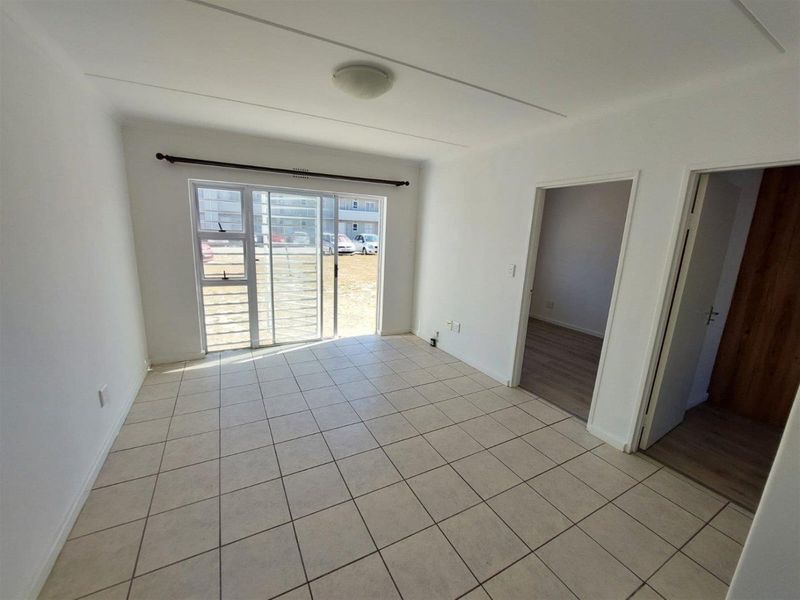 An empty, open-plan living area featuring neutral tiled flooring and a sliding glass door with a security gate leading to the exterior.