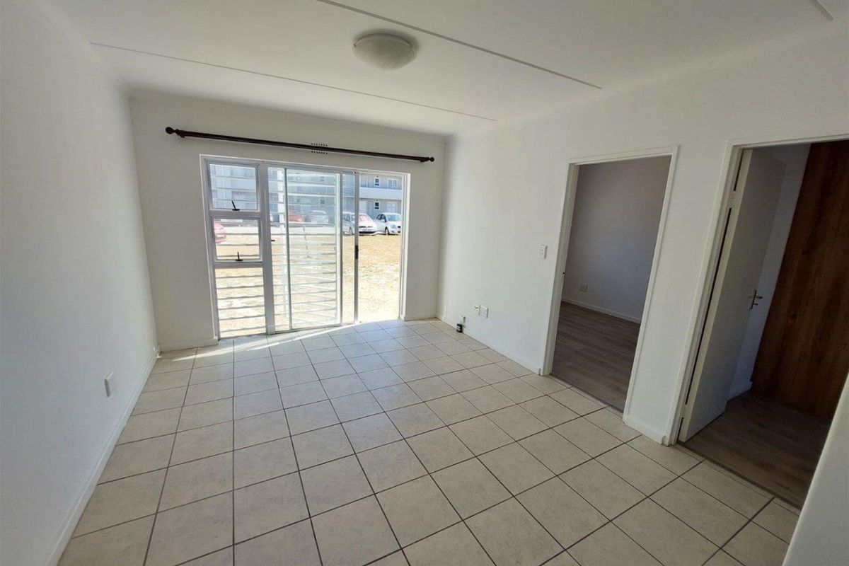 An empty, open-plan living area featuring neutral tiled flooring and a sliding glass door with a security gate leading to the exterior.