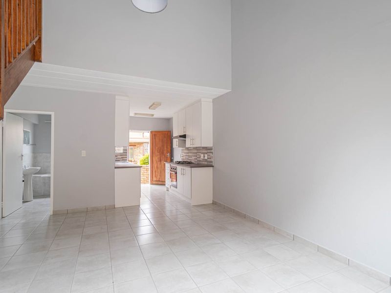 Open-plan living area featuring tiled flooring, a modern kitchen with built-in appliances, and a wooden staircase leading to the upper level.