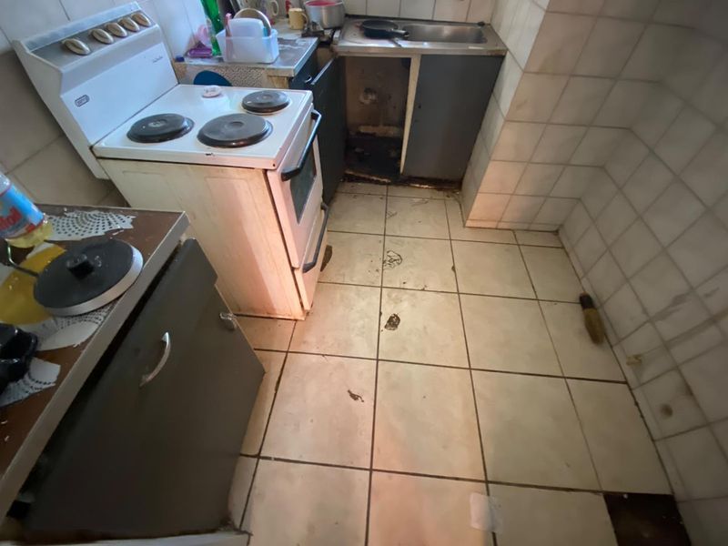 A dated kitchen featuring a freestanding stove, stainless steel sink, and tiled surfaces, currently requiring significant maintenance and renovation to restore functionality.