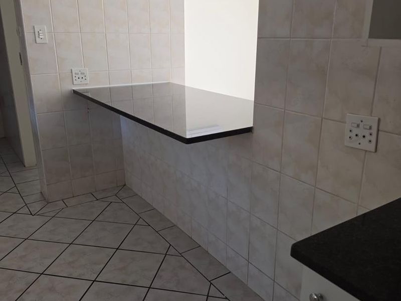 A clean kitchen area featuring tiled flooring, a granite breakfast bar, and a wall-mounted air conditioning unit.