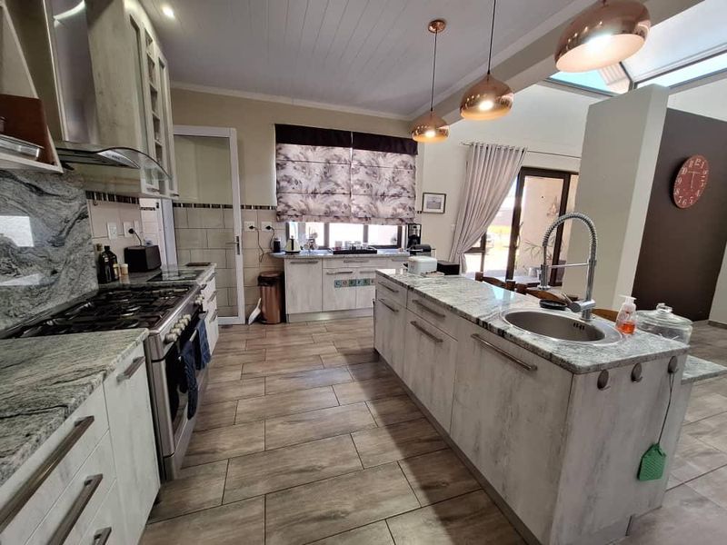 Modern open-plan kitchen featuring a large island with granite countertops, gas hob, and contemporary pendant lighting, seamlessly flowing into the living area.