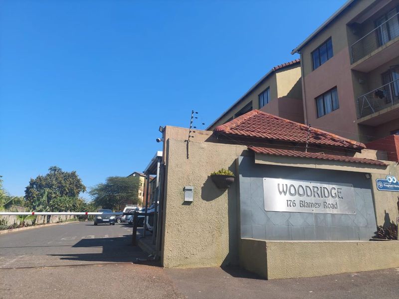 The entrance to Woodridge apartment complex, featuring a secure gated access point with electric fencing and clear signage.