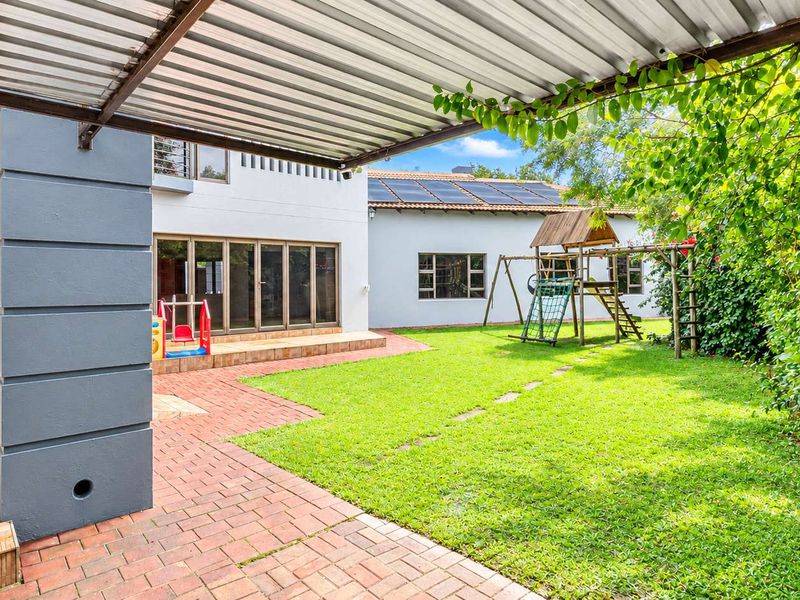 A spacious rear garden featuring a covered brick-paved patio, lawn area, and solar panels installed on the main roof structure.