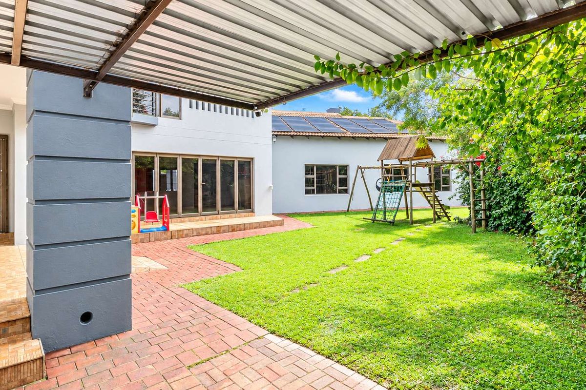 A spacious rear garden featuring a covered brick-paved patio, lawn area, and solar panels installed on the main roof structure.