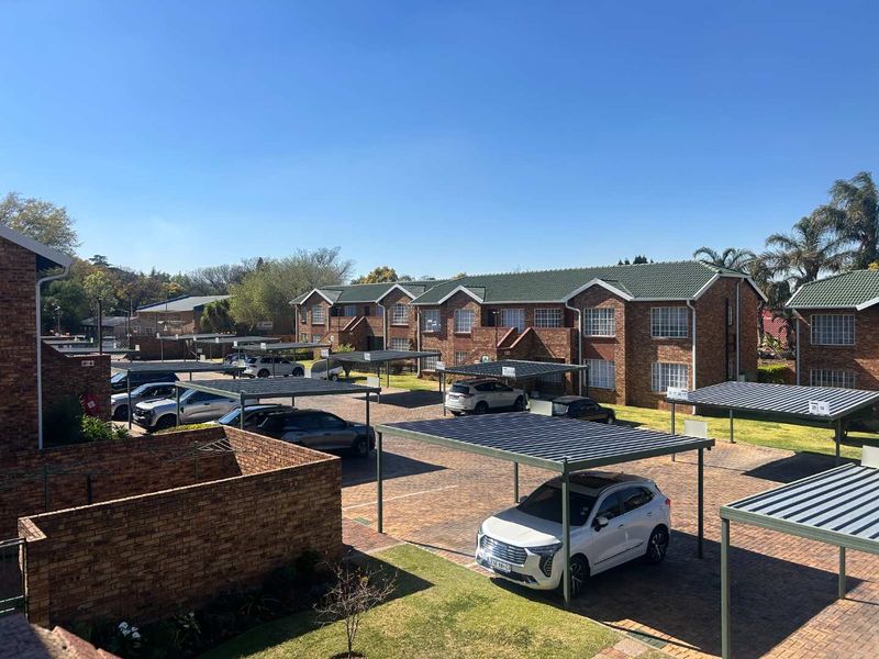 An elevated view of a townhouse complex featuring brick buildings, tiled roofs, and multiple covered carport parking bays within a paved courtyard setting.