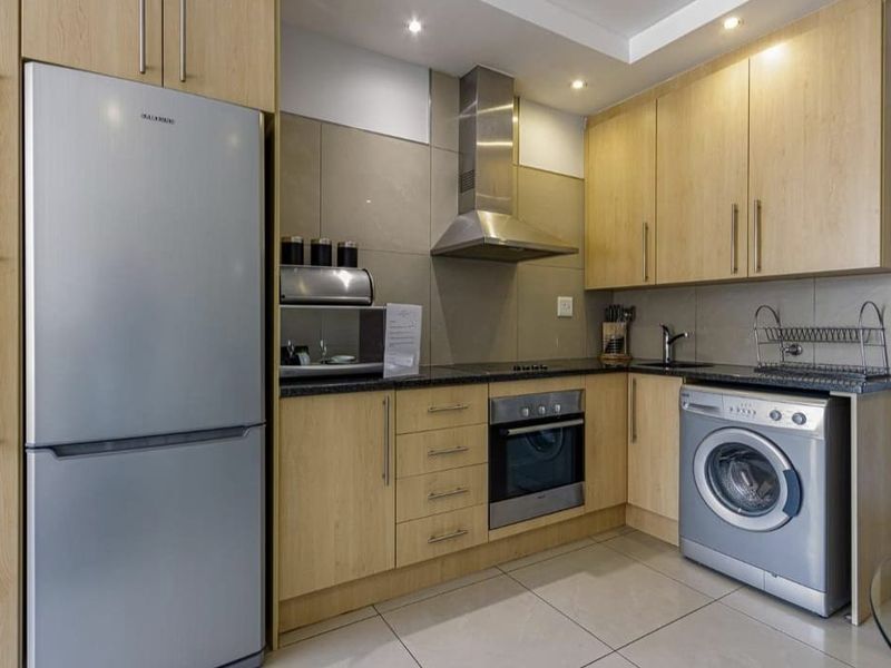Modern kitchen featuring light wood cabinetry, stainless steel appliances, integrated oven and hob, tiled backsplash, and sleek tiled flooring.