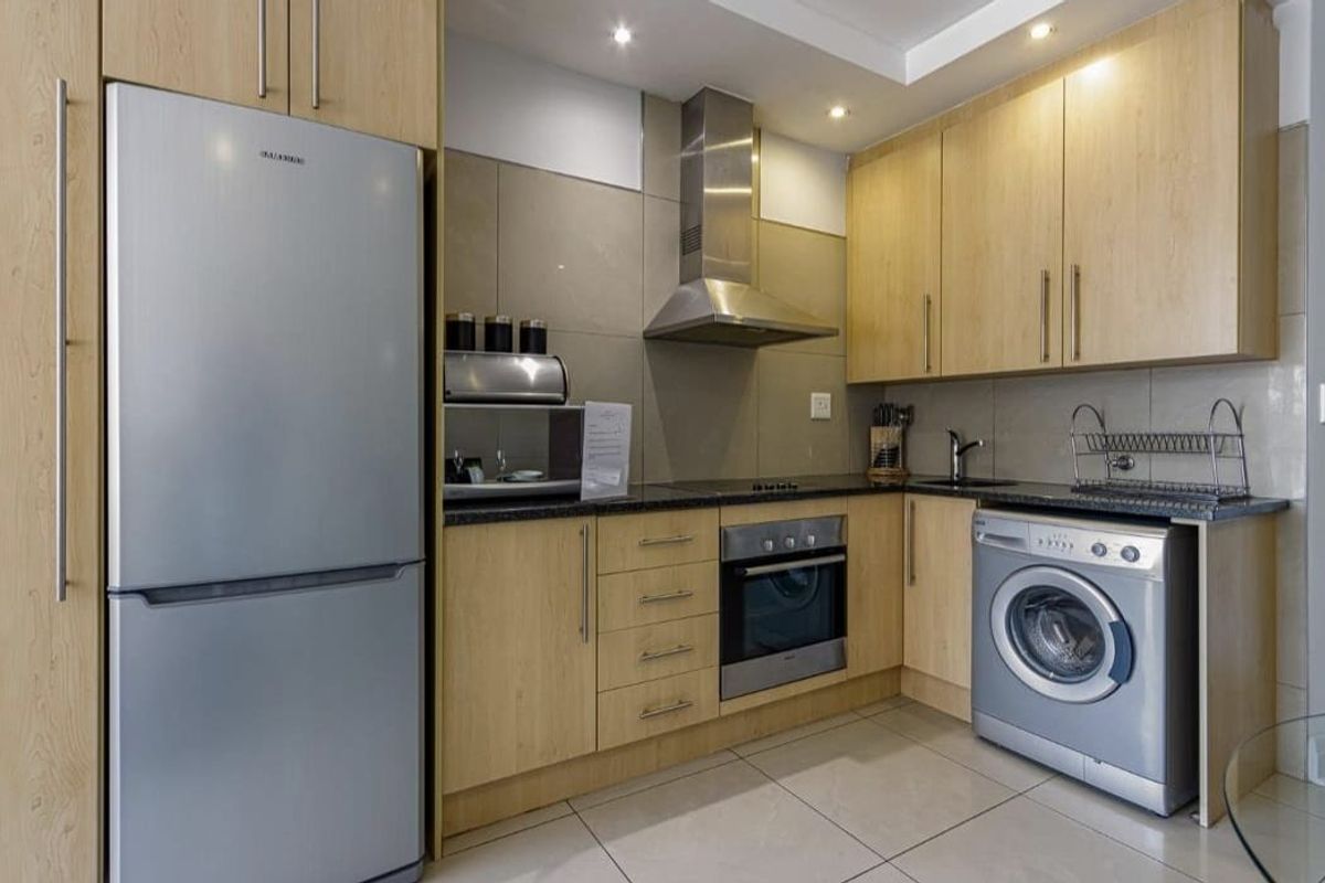 Modern kitchen featuring light wood cabinetry, stainless steel appliances, integrated oven and hob, tiled backsplash, and sleek tiled flooring.