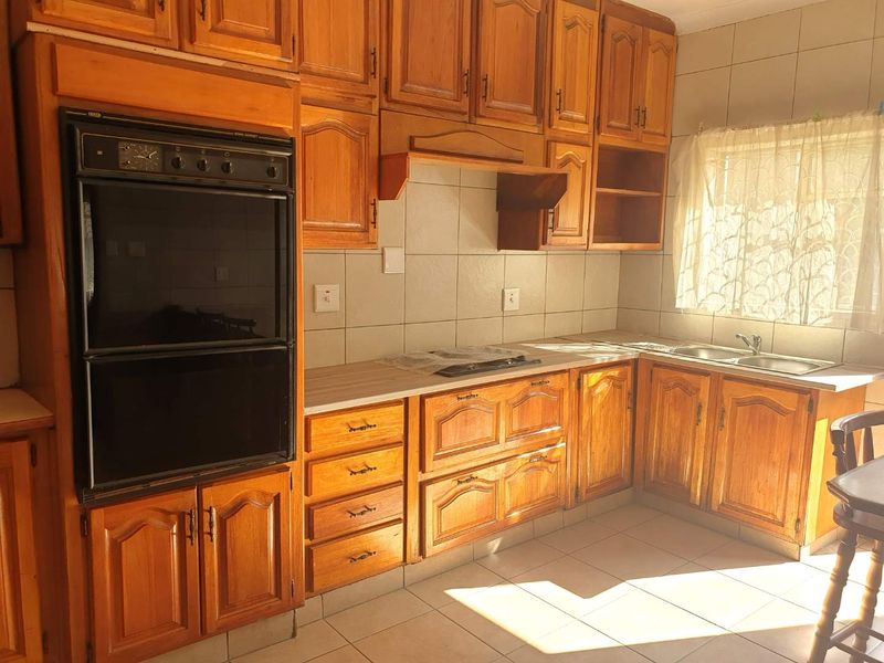 A functional kitchen featuring traditional wooden cabinetry, a built-in double oven, electric hob, and a double basin sink with tiled finishes.