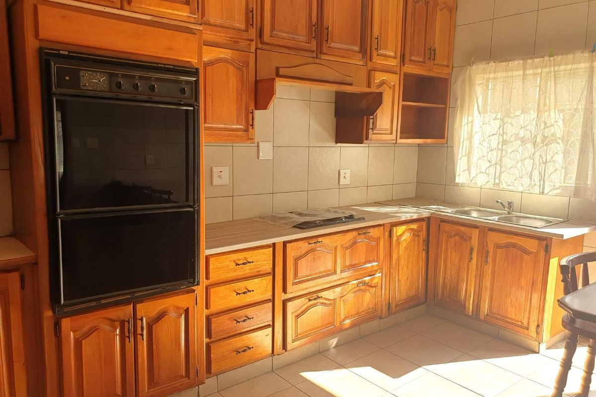 A functional kitchen featuring traditional wooden cabinetry, a built-in double oven, electric hob, and a double basin sink with tiled finishes.