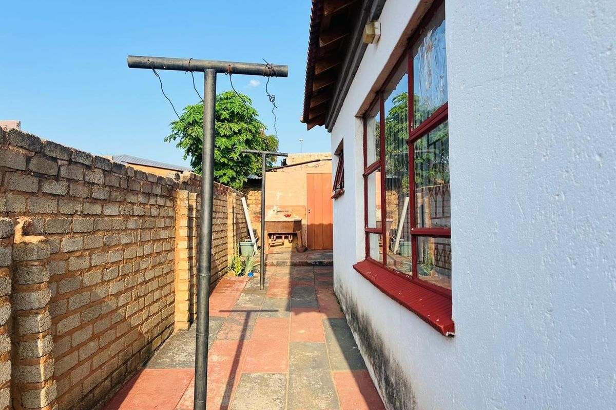 A side exterior view of the property featuring a paved pathway, brick boundary wall, and metal washing line infrastructure.