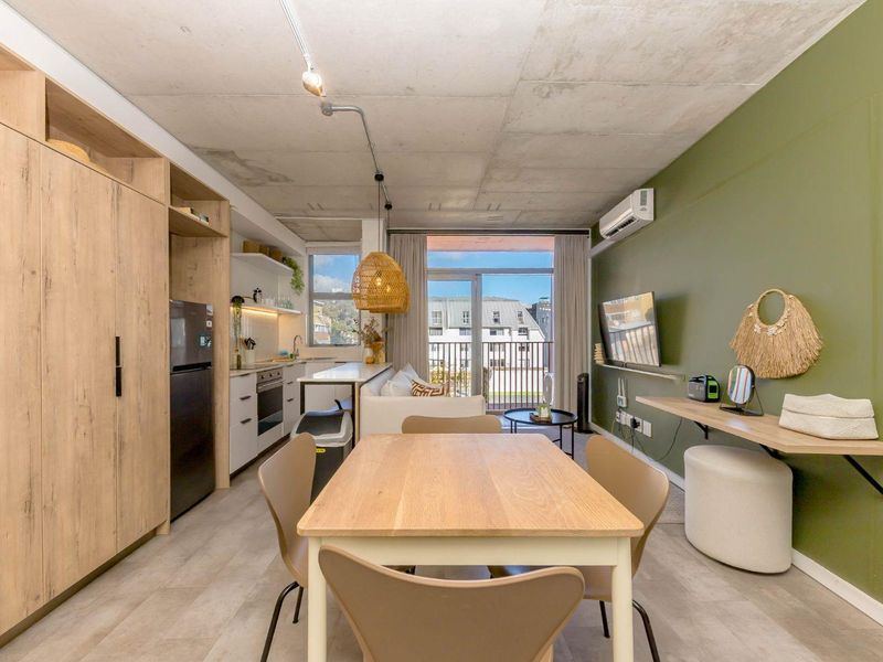 Modern open-plan living area featuring an exposed concrete ceiling, sleek kitchen cabinetry, and direct access to a private balcony.