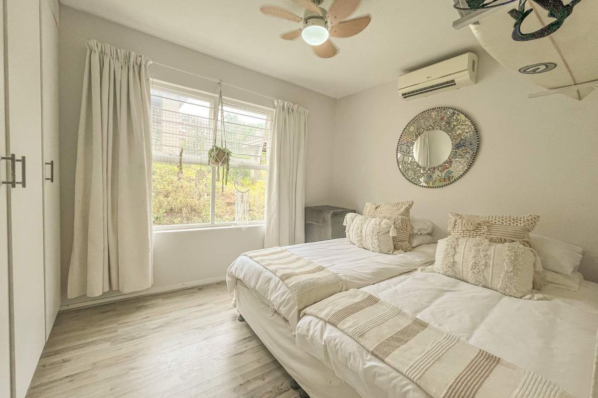 A bright bedroom featuring light wood-look flooring, built-in wardrobes, a ceiling fan, and a wall-mounted air conditioning unit.