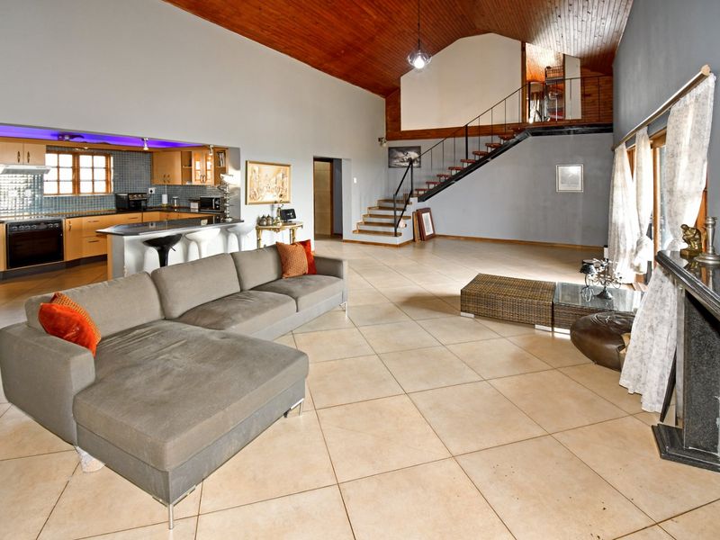 Spacious open-plan living area featuring a vaulted timber ceiling, tiled floors, a modern kitchen with island, and a staircase leading to an upper level.