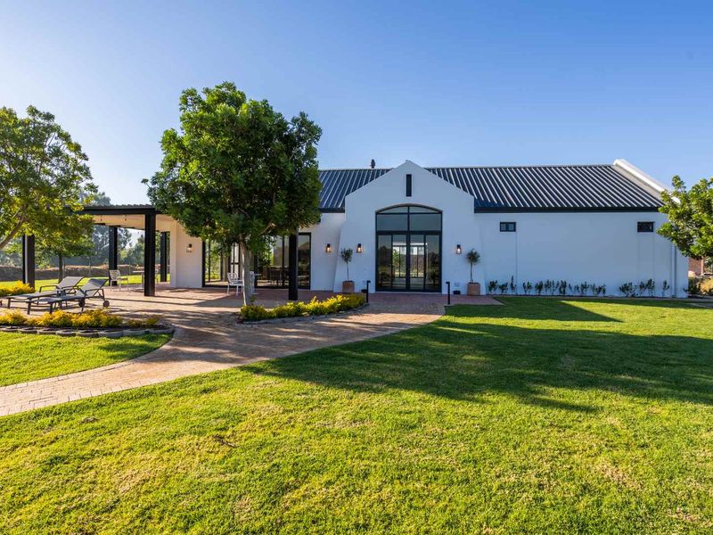 A beautifully maintained rear exterior view featuring a modern white facade, black metal roof, covered patio area, and expansive landscaped garden.