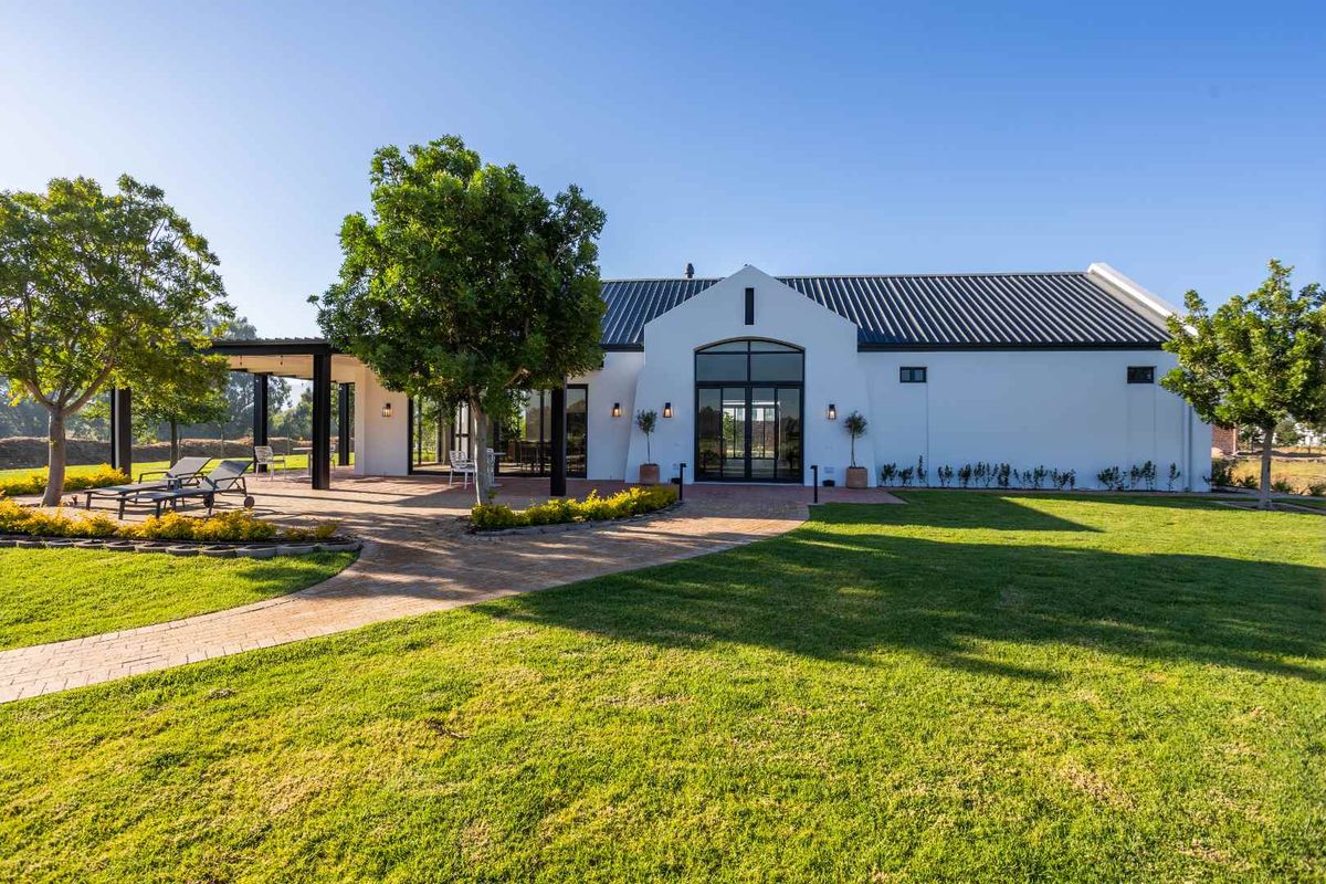 A beautifully maintained rear exterior view featuring a modern white facade, black metal roof, covered patio area, and expansive landscaped garden.
