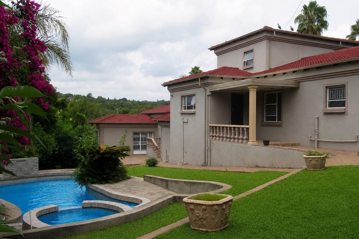 Rear view of the house featuring a swimming pool, landscaped garden, and a covered patio area with classic architectural detailing.