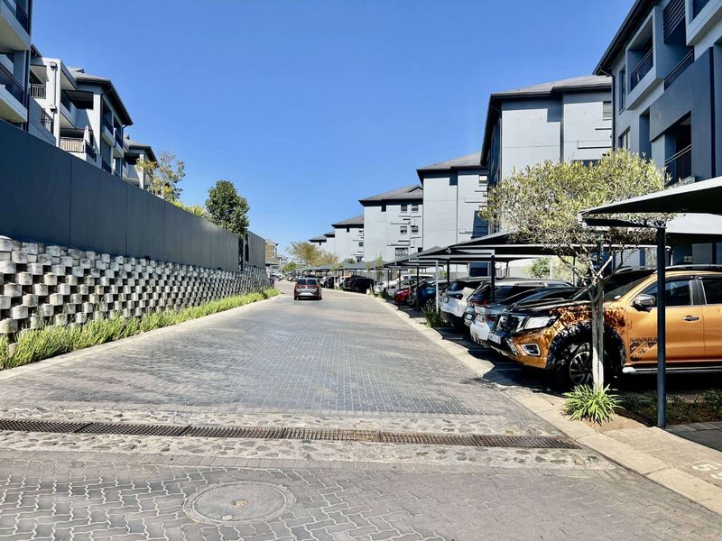 A well-maintained apartment complex driveway featuring paved surfaces, covered parking bays, and modern multi-story residential buildings.