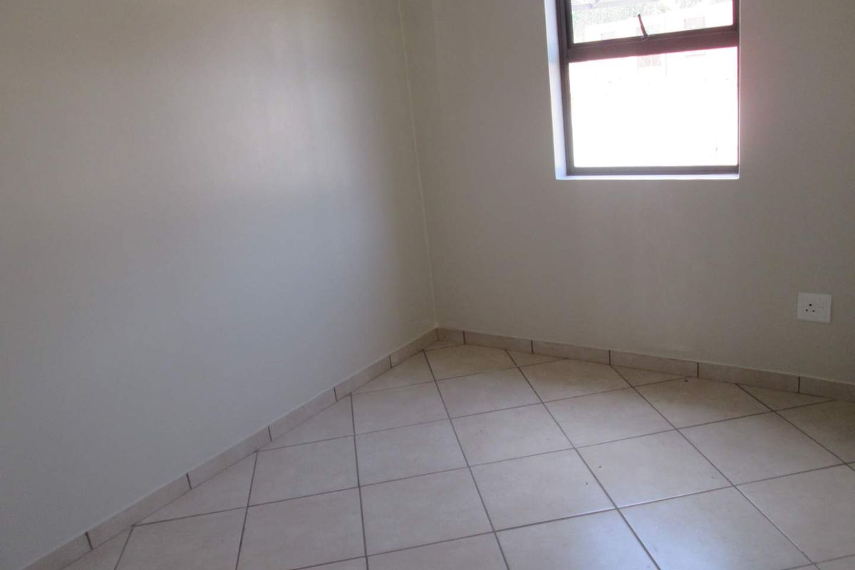 A clean, empty bedroom featuring neutral tiled flooring, plain walls, and a window providing natural light.