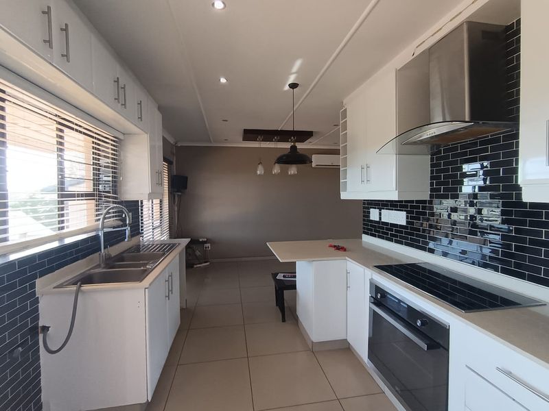 Modern kitchen featuring white cabinetry, black subway tile backsplash, integrated stainless steel appliances, and tiled flooring with recessed lighting.