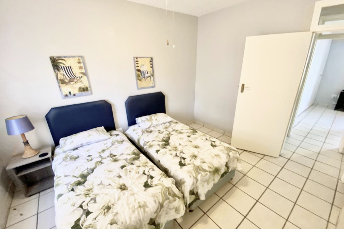 A functional bedroom featuring neutral wall finishes, tiled flooring, and a ceiling fan, providing a clean and simple living space.
