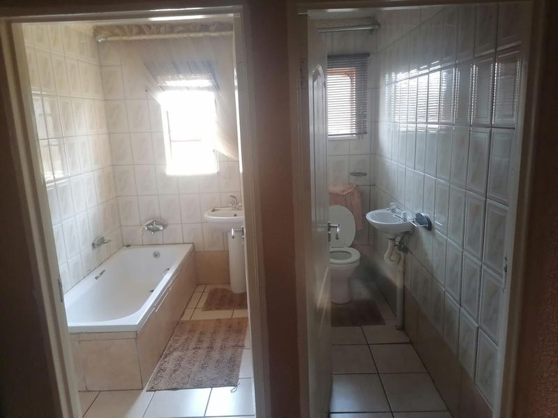 A split-view bathroom featuring a bathtub, pedestal basin, and toilet with tiled walls and floors, showing dated finishes and exposed plumbing.