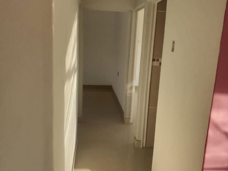 A clean, empty hallway featuring neutral tiled flooring and coved ceilings, providing access to adjacent rooms within the property.