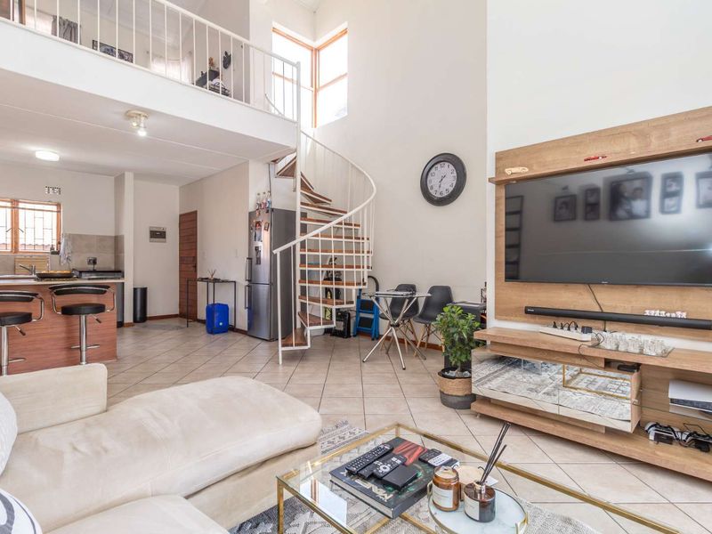 Spacious open-plan living area featuring a spiral staircase leading to a mezzanine level, tiled floors, and a functional kitchen with a breakfast bar.