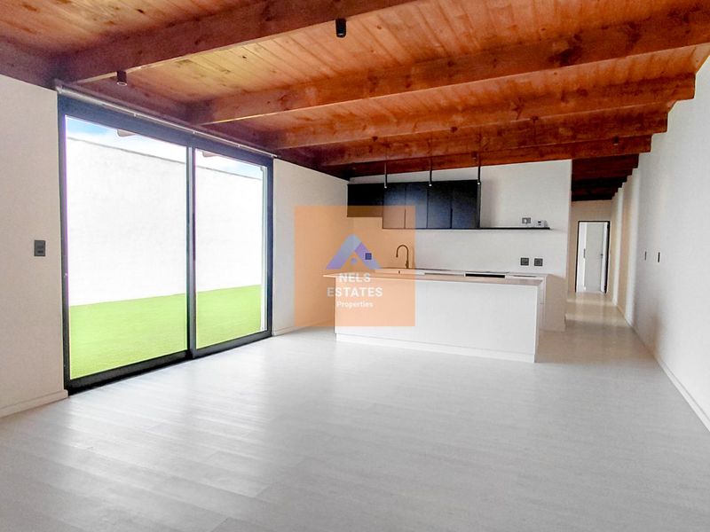 Modern open-plan living and kitchen area featuring exposed timber ceiling beams, sleek cabinetry, and large sliding glass doors leading to an outdoor space.