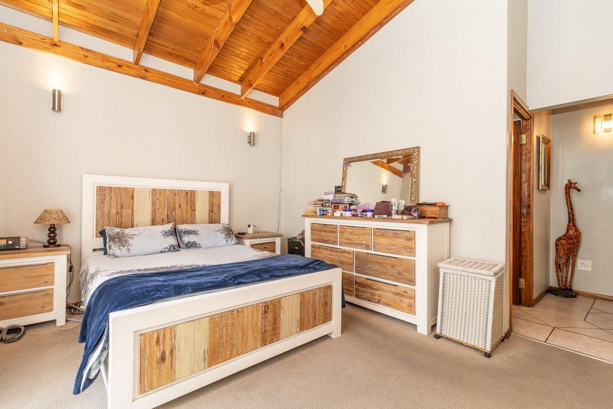 A spacious bedroom featuring a high vaulted timber-beamed ceiling, neutral carpeting, and wall-mounted lighting fixtures.