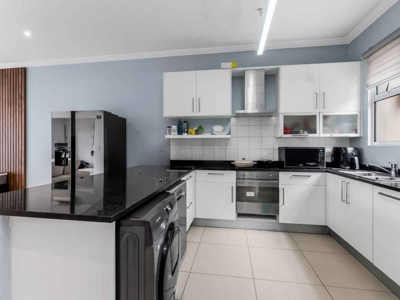 Modern kitchen featuring white cabinetry, black granite countertops, stainless steel appliances, and a convenient breakfast bar, set against a neutral backdrop.