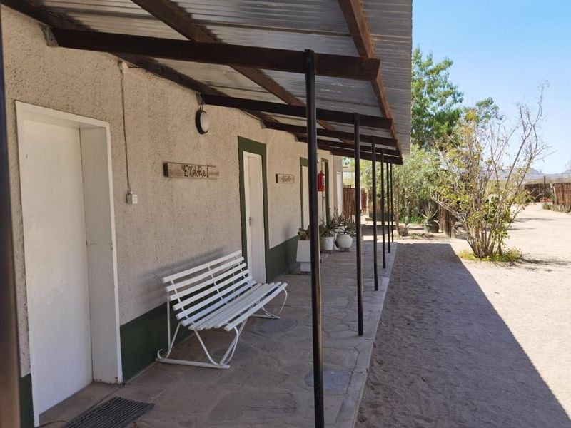 A covered outdoor patio area with stone flooring, metal support posts, and a corrugated roof, providing access to multiple guest room entrances.