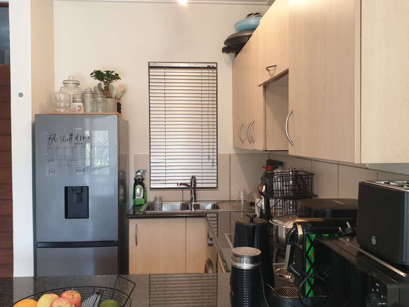 A functional kitchen featuring light wood-tone cabinetry, granite countertops, a stainless steel double sink, and a tiled backsplash with venetian blinds.
