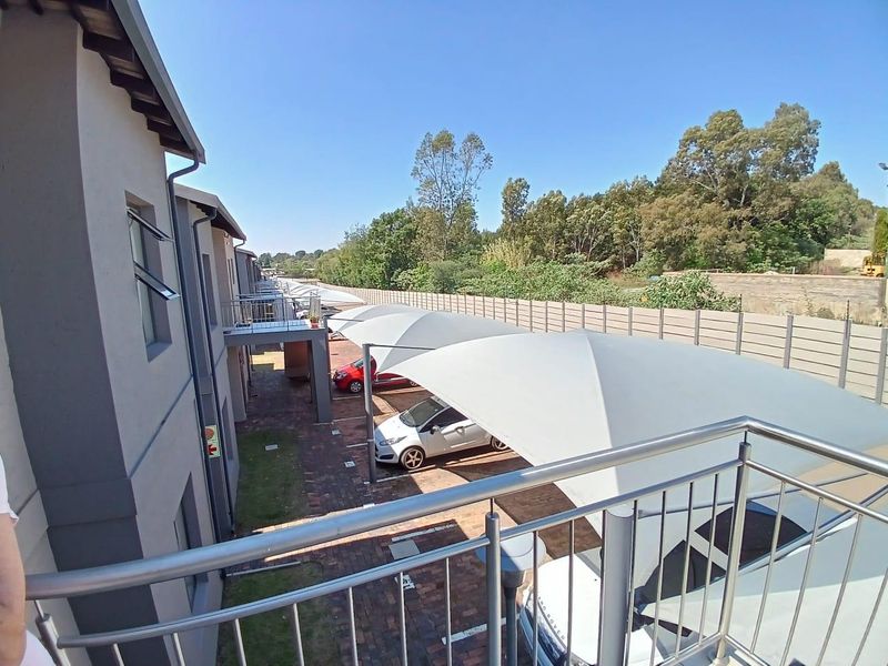 View from an upper-level balcony overlooking a paved parking area with modern shade sail carports and a secure boundary wall.