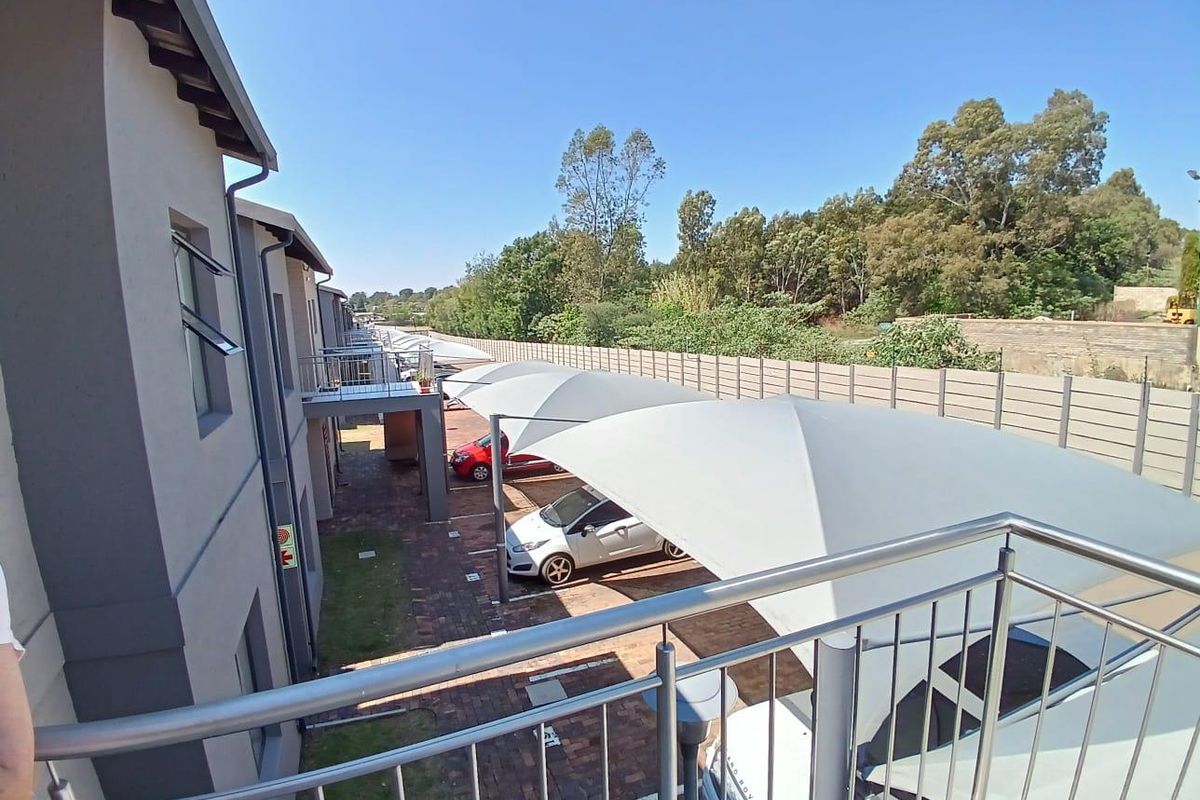 View from an upper-level balcony overlooking a paved parking area with modern shade sail carports and a secure boundary wall.
