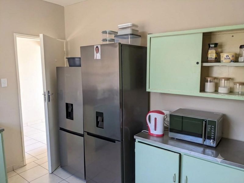 A functional kitchen area featuring dated light green built-in cabinetry, a stainless steel countertop, and tiled flooring.